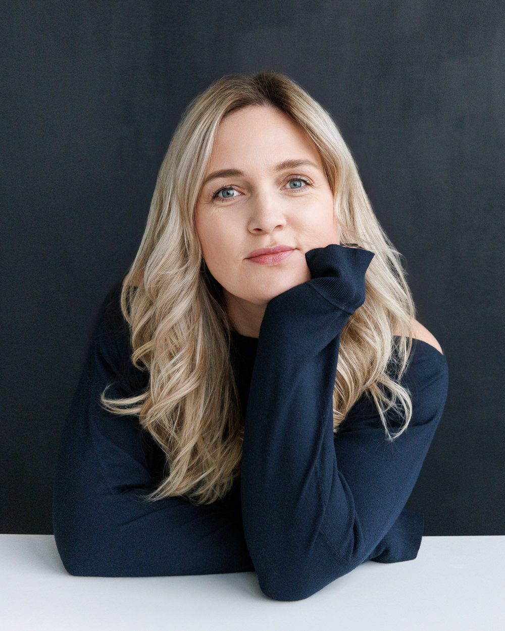 Author brand portrait featuring a relaxed pose and soft smile, styled in a dark top with a minimal black background, captured in Calgary by Kate Daniel Photography.