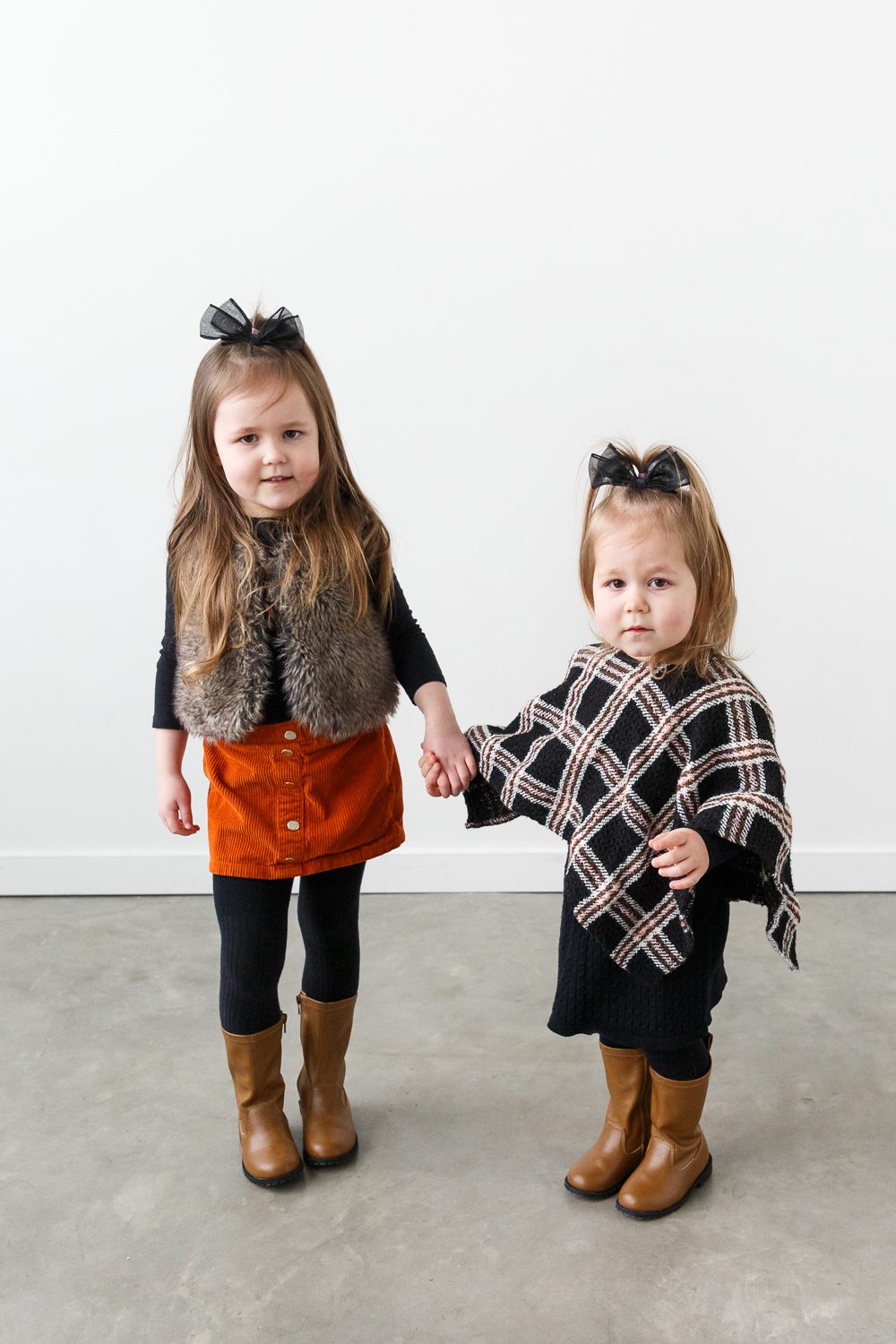 Two young children wearing stylish fall outfits and holding hands, photographed in a minimalist studio space for a kid-focused brand session – Calgary brand photography by Kate Daniel Photography